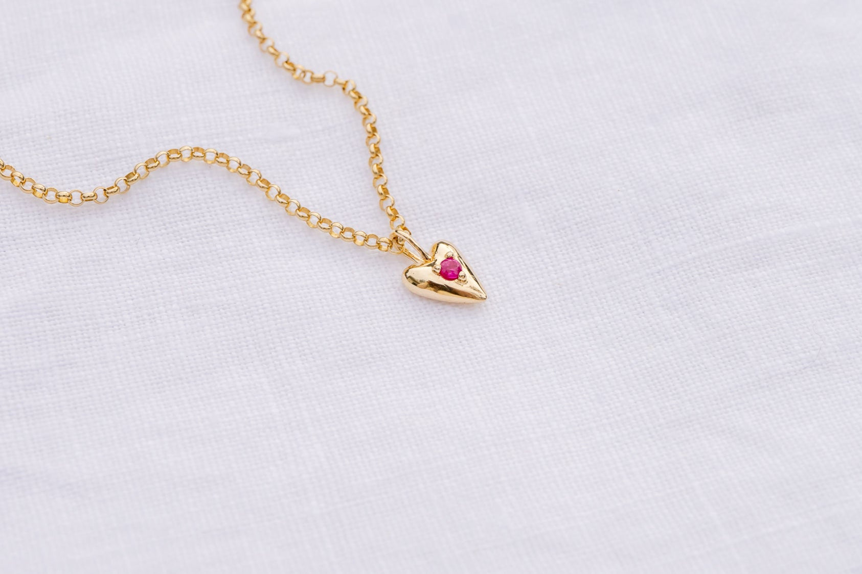 Gold necklace with a heart-shaped pendant on a light gray background