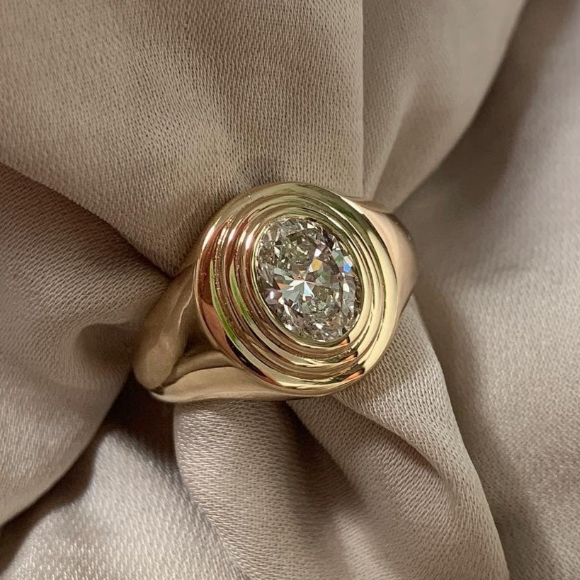 GOLD SIGNET RING WITH AN OVAL DIAMOND AND CONCENTRIC STEPS AROUND THE DIAMOND